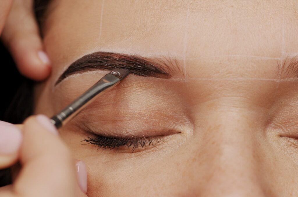 Frau bei der Augenbrauenfärbung. Professionelle Färbung der weiblichen Augenbrauen in einem Schönheitssalon. Nahaufnahme des Gesichts der Kundin und der Hände der Stylistin bei der Arbeit. Konzept der Schönheitspflege.