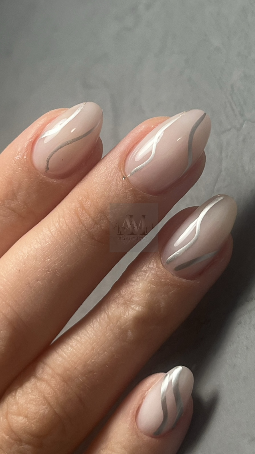 Eine Hand mit elegant manikürten Nägeln in Beige mit silbernen Streifen.