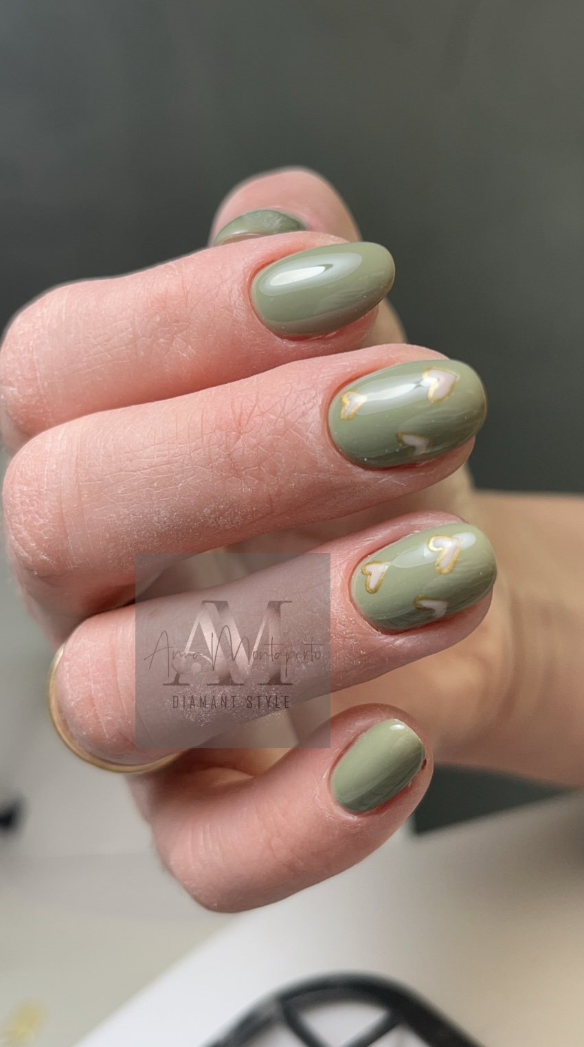 Nahaufnahme einer Hand mit olivfarbenen Nagellack und goldenen Akzenten