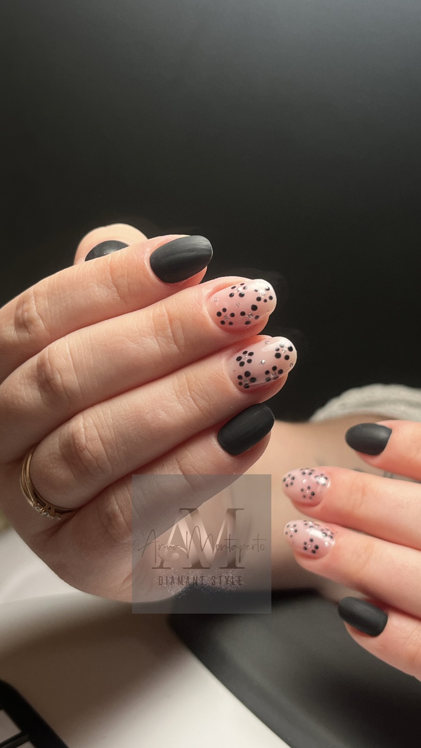 Hände mit schwarzem und gepunktetem Nageldesign in eleganter Pose.