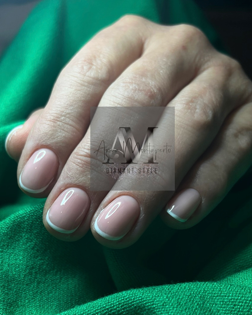 Eine Hand mit gepflegten French Nails auf einem grünen Stoff.