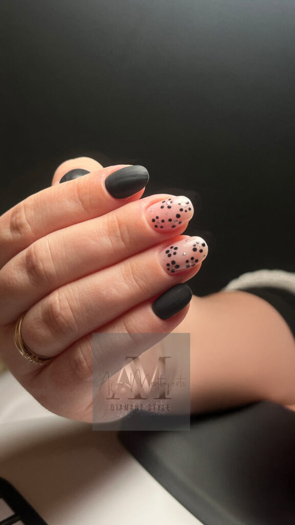 Eine Hand mit mattschwarzen Nägeln und zwei Nägeln mit schwarzem Punktemuster
